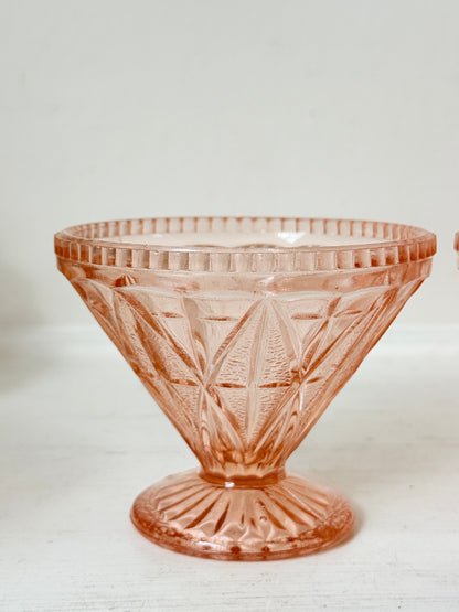 A vintage pink cut-glass pedestal bowl with a fluted rim and geometric diamond pattern, set against a plain off-white background.