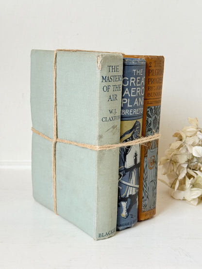Vintage decorative book bundle in blue, grey, and ochre tied with twine, photographed on a white surface