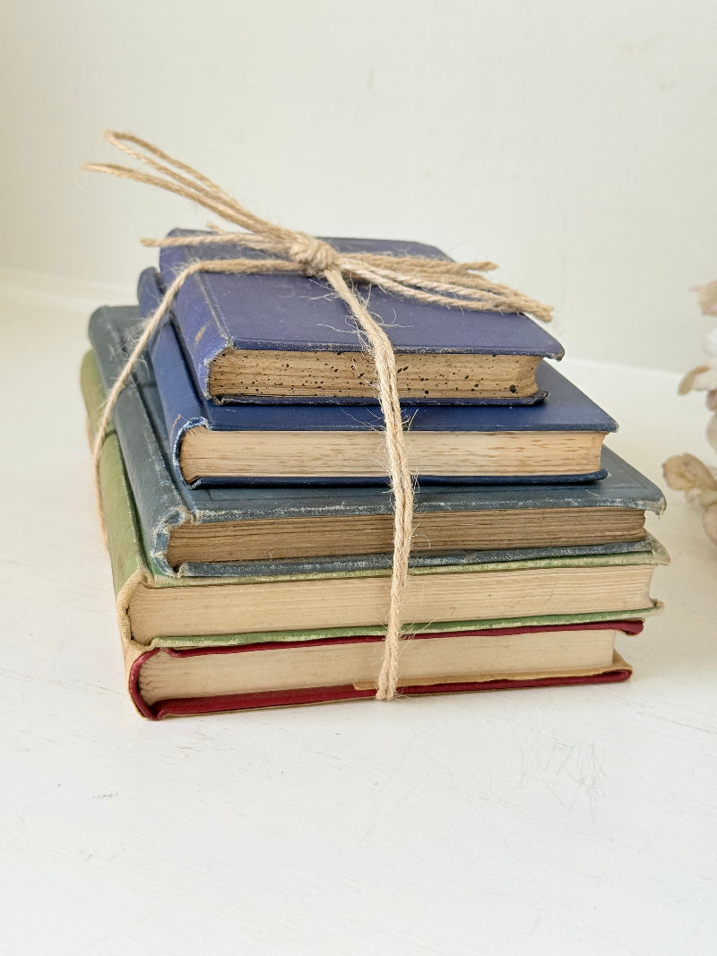Vintage decorative book bundle in blue and green tied with twine, photographed on a white surface