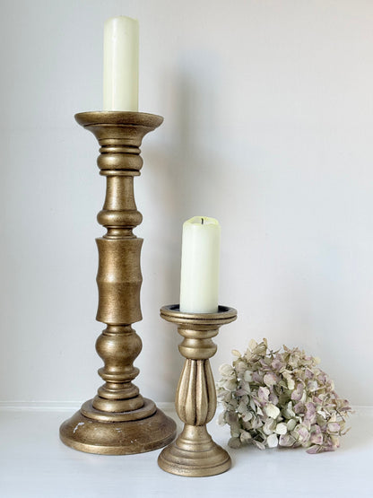 Pair of vintage wooden candlesticks, one tall and one small, in golden-toned finish, styled with pillar candles on a white surface.