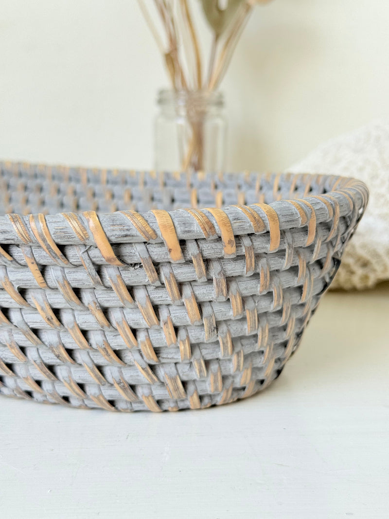 Vintage grey woven bread basket with oval shape and raised rim, photographed on white surface.