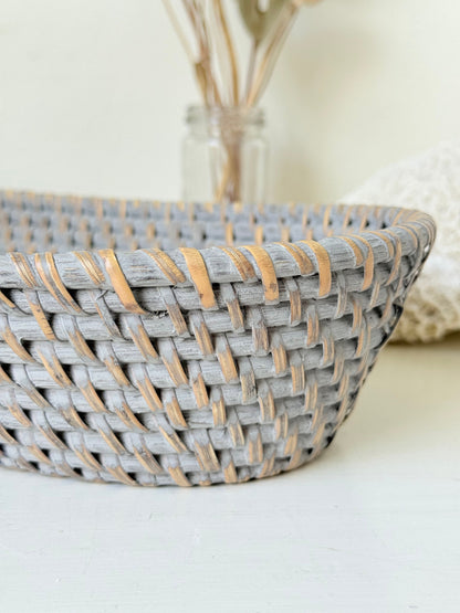 Vintage grey woven bread basket with oval shape and raised rim, photographed on white surface.