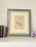 Framed cockatoo bird print in green and gold frame with mount, styled on white surface with vintage books