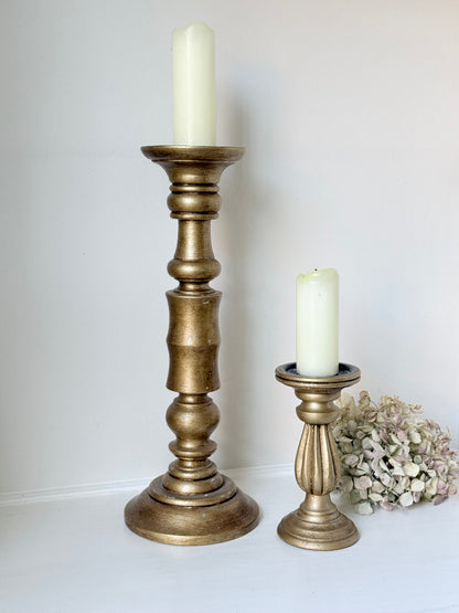 Pair of vintage wooden candlesticks, one tall and one small, in golden-toned finish, styled with pillar candles on a white surface.