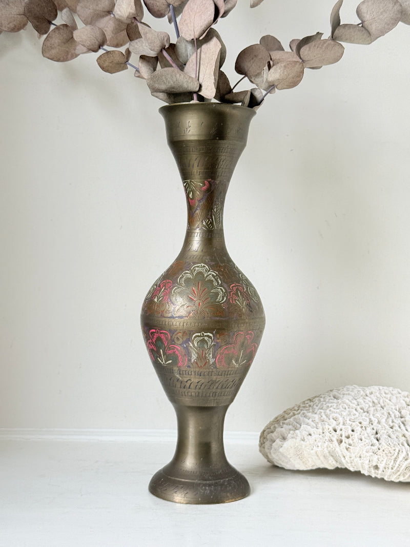 Vintage Indian engraved brass vase with enamel floral decoration and aged patina styled with dried stems on white surface