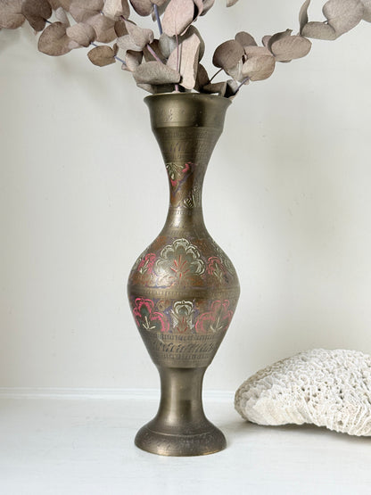 Vintage Indian engraved brass vase with enamel floral decoration and aged patina styled with dried stems on white surface
