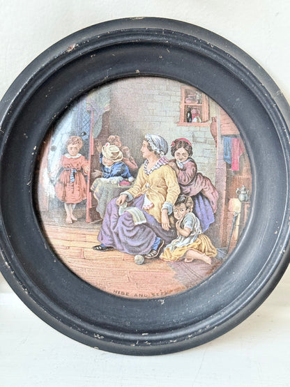 Antique Prattware pot lid in black round frame with Victorian family scene on white surface.