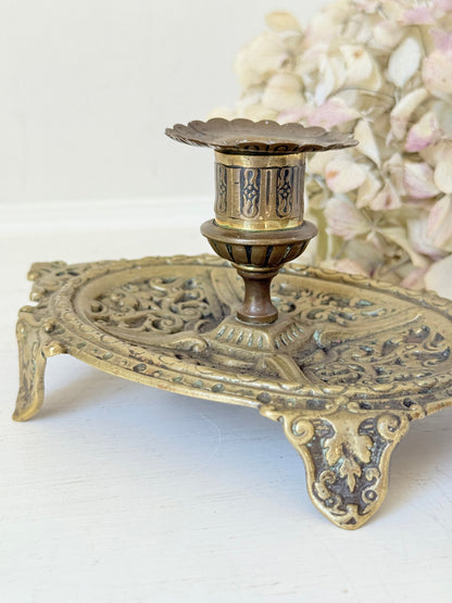 Ornate vintage brass candlestick with decorative handle and footed base, photographed on a white surface