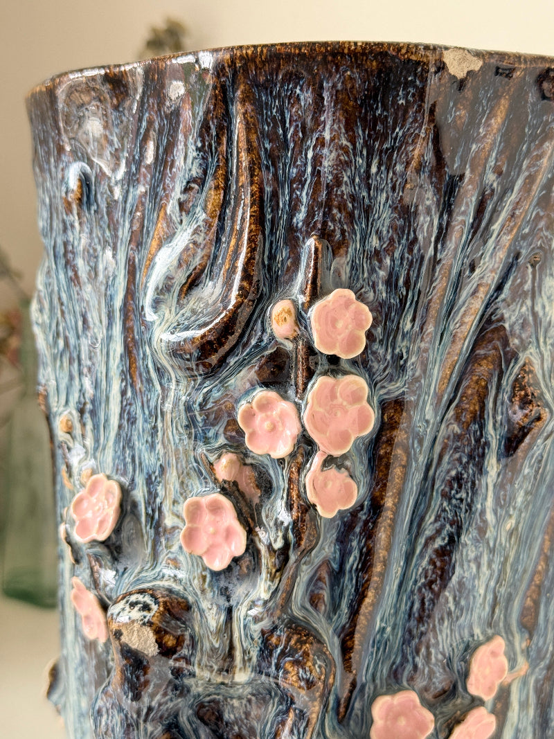 Large ceramic tree trunk vase with applied pink cherry blossom detail, textured bark form and dark drip glaze