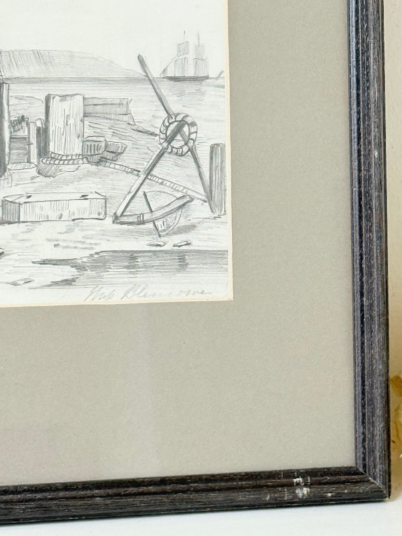 Vintage pencil drawing of rural scene with outbuildings and figures, under glass in black wooden frame, photographed on white surface.
