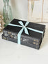 Three antique black books with decorative spines tied with a striped cotton ribbon on a white surface, styled with glass bottles