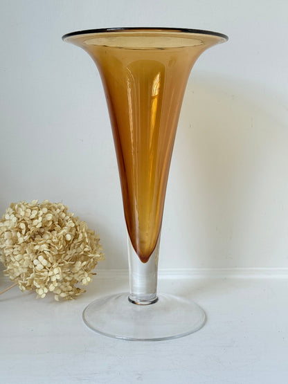 Tall mid-century amber trumpet vase with flared rim and clear glass foot, styled against a neutral background
