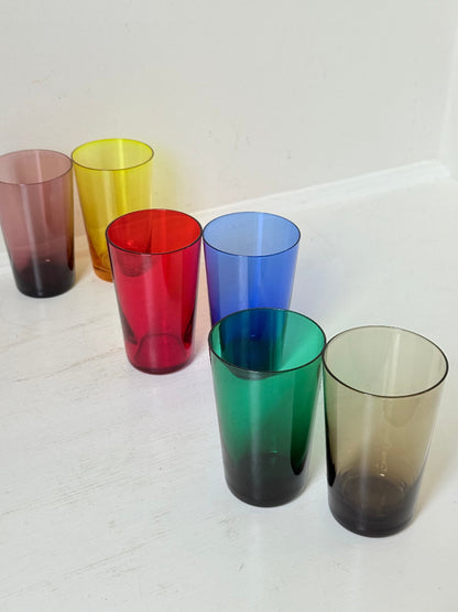 Set of six mid-20th century Boussu coloured glass beakers in rainbow hues, green with original label, photographed on white surface.