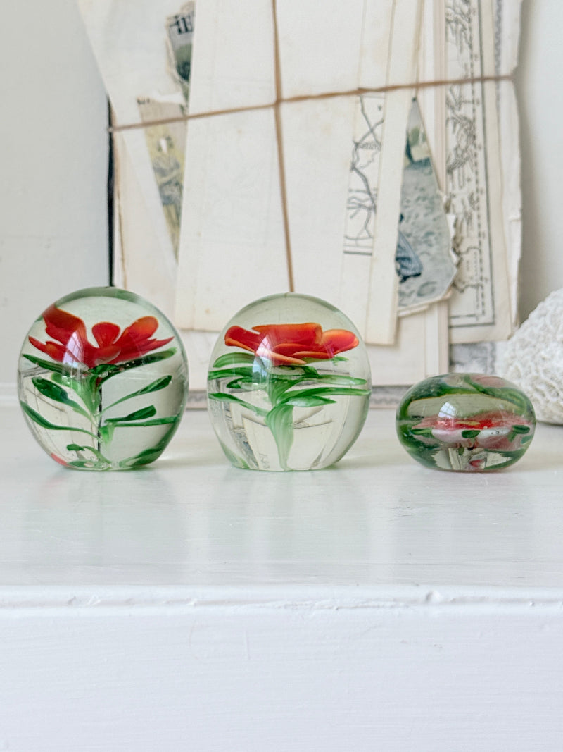 Trio of vintage glass paperweights with hand worked red floral detail, clear glass domes and green leaf decoration
