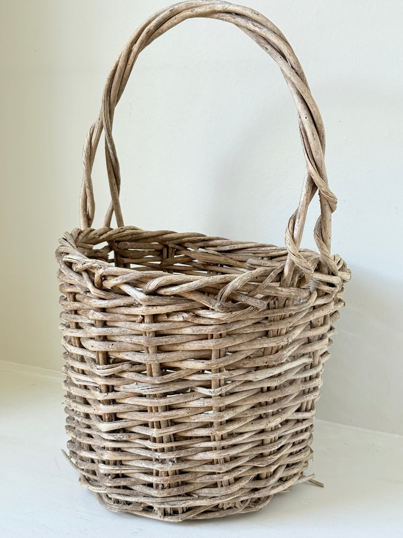 Rustic vintage wicker basket with woven handle and aged natural finish photographed on a white surface