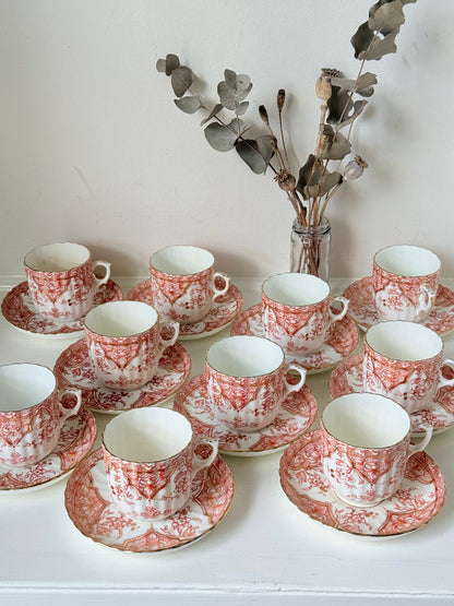 Vintage coral transferware coffee cans and saucers with scalloped edges and gold accents, set of ten, styled on a white surface.