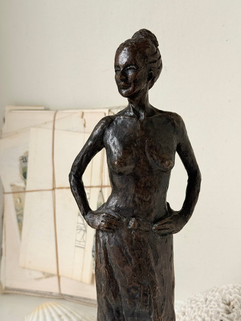 Solid bronze figure of a standing semi nude woman with upswept hair on a white marble base
