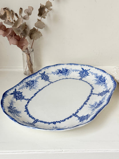 Antique oval blue and white platter with floral border photographed on a white surface