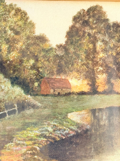 Antique framed rural watercolour of river, trees, and red-roofed building, in dark wooden frame with cream mount, on white surface.