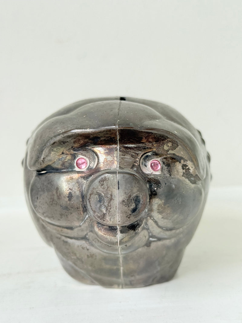 Vintage cast metal piggy bank in the shape of a pig with red painted eyes, photographed on a white surface