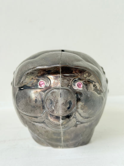 Vintage cast metal piggy bank in the shape of a pig with red painted eyes, photographed on a white surface