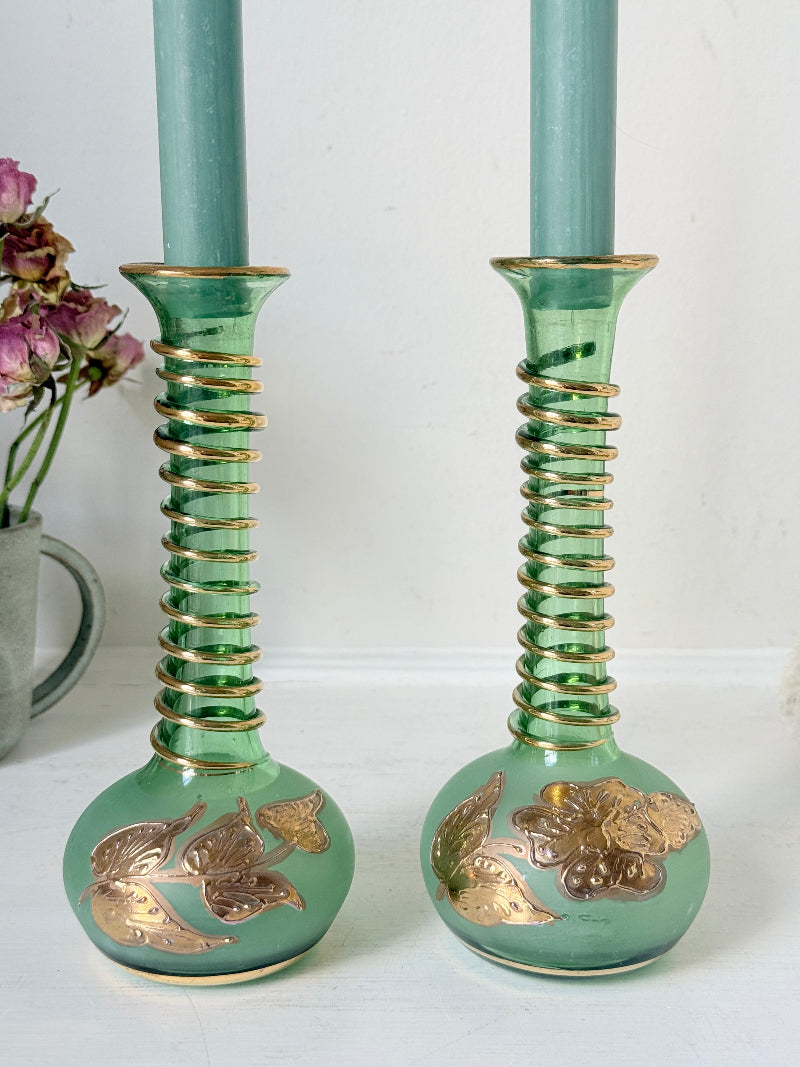 Pair of vintage green glass candlesticks with gold detail and spiral stems styled with blue taper candles on white surface