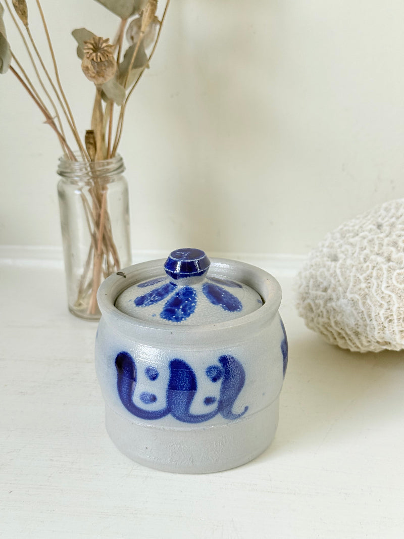 Vintage lidded pottery jar with hand painted blue floral decoration, photographed on a white surface