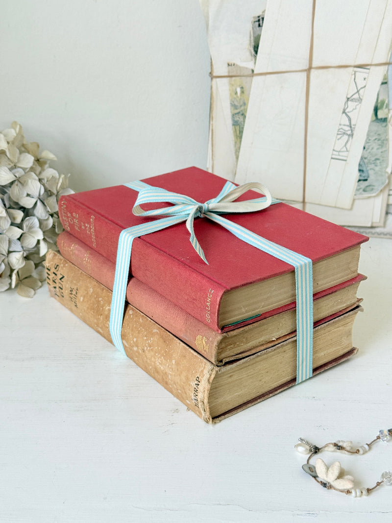 Three antique red books with aged spines tied with a turquoise striped ribbon on a white surface, styled with glass and beads