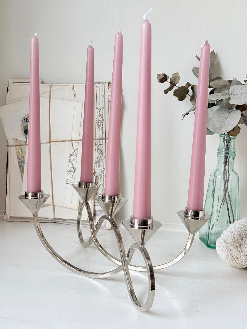 Silver tone five light candelabra with a sculptural looped base holding pink candles, photographed on a white surface