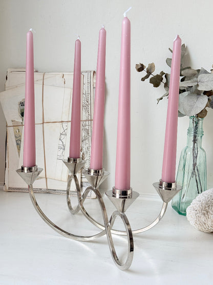 Silver tone five light candelabra with a sculptural looped base holding pink candles, photographed on a white surface