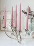 Silver tone five light candelabra with a sculptural looped base holding pink candles, photographed on a white surface