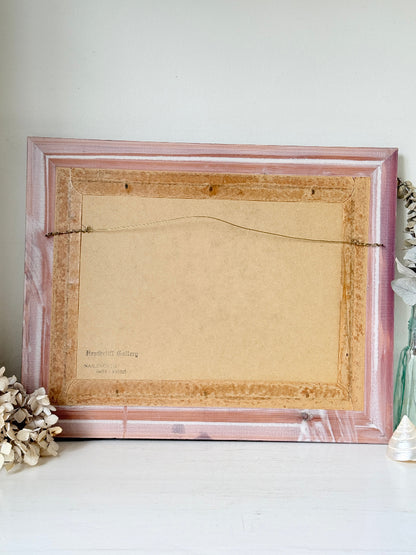 The back of a rectangular picture frame with a distressed pink and white marble-look finish, showing a tan cardboard backing and hanging wire, set against a light gray wall.
