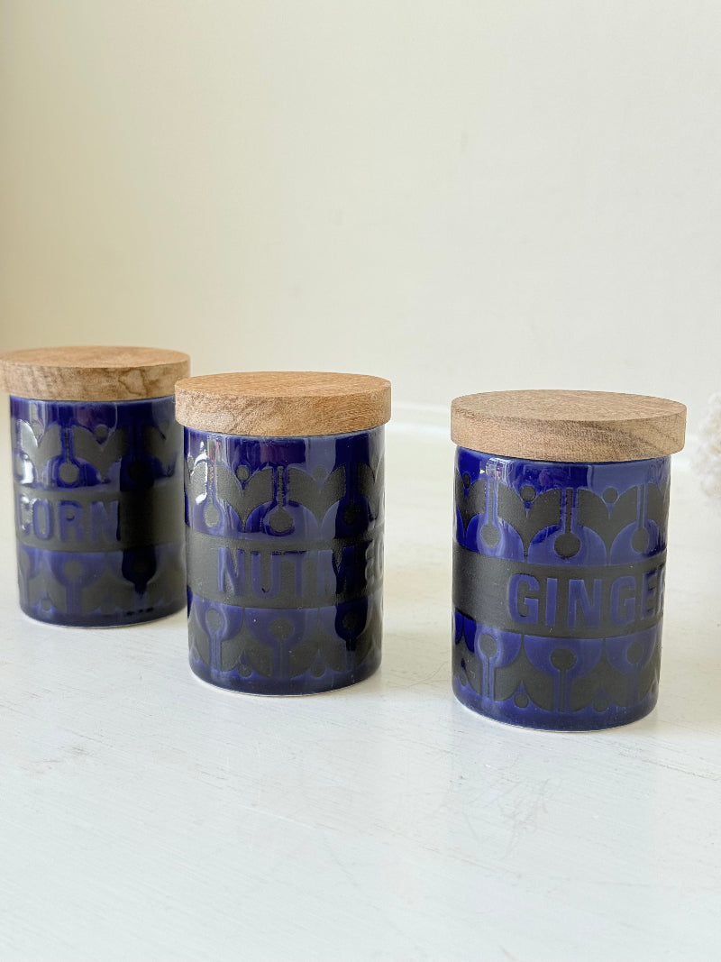 Set of three Hornsea Pottery spice jars in cobalt blue with wooden lids, labelled Ginger, Nutmeg, and Peppercorn, photographed on white surface

