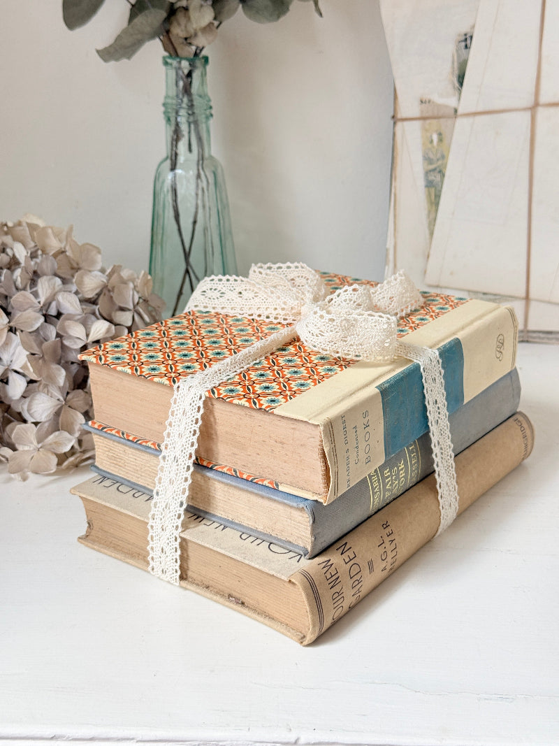 Bundle of vintage cream and blue cloth books with one patterned cover tied with ivory lace for shelf styling