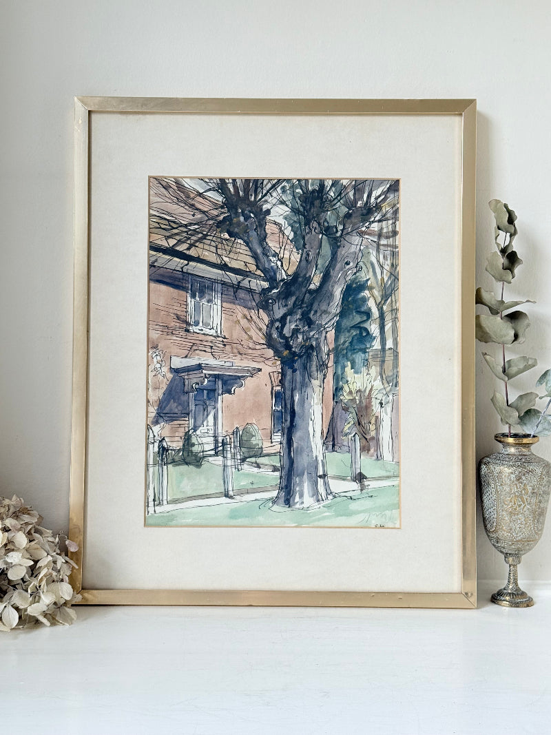 Framed vintage watercolour painting of a large tree and brick house, photographed on a white surface.