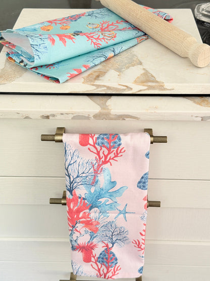 Pale pink coral and seaweed print cotton tea towel with wooden spoon on a marble surface