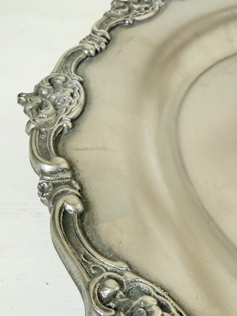 Vintage silvertone metal tray with ornate border, photographed on a white surface