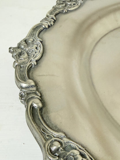 Vintage silvertone metal tray with ornate border, photographed on a white surface