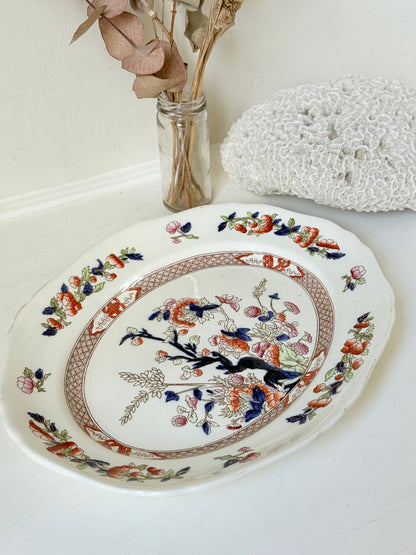 Vintage oval serving platter with chinoiserie style blue and red pattern photographed on a white surface