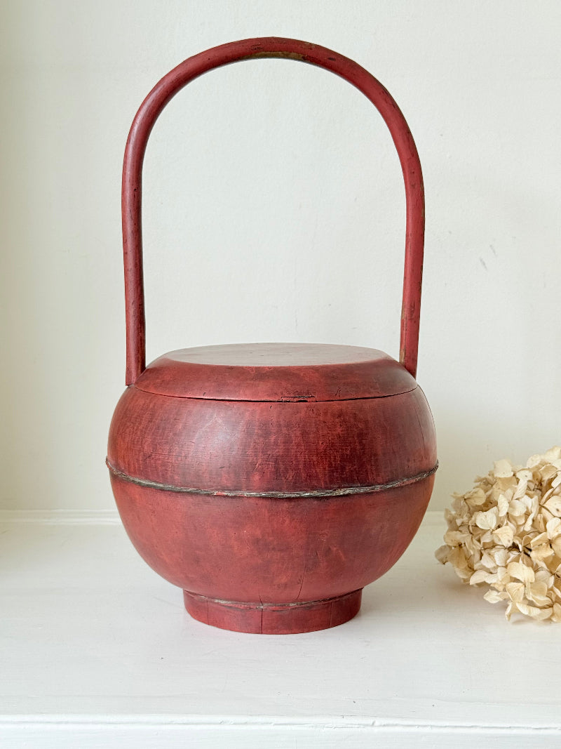 Vintage red painted wooden basket with tall curved handle and domed lid photographed on a white surface