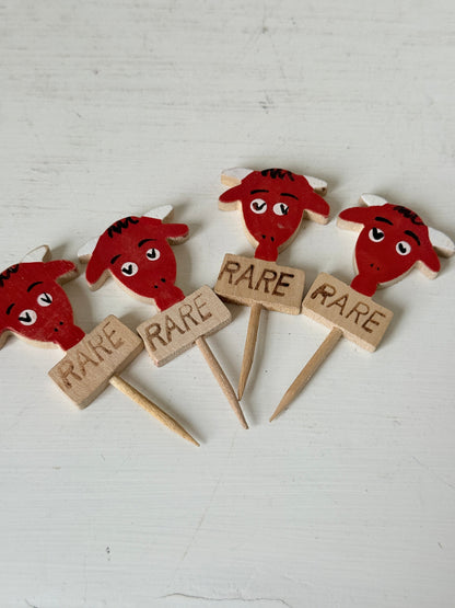 Vintage hand painted wooden steak markers on cocktail sticks labelled rare medium and well done, photographed on a white surface