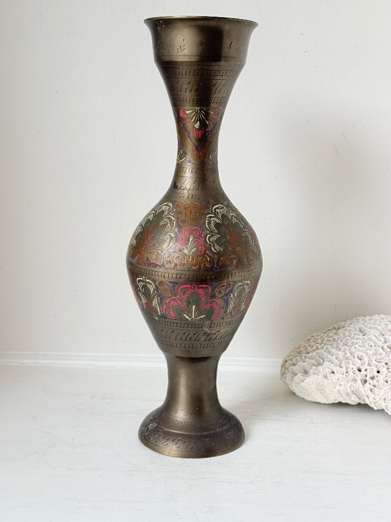 Vintage Indian engraved brass vase with enamel floral decoration and aged patina styled with dried stems on white surface