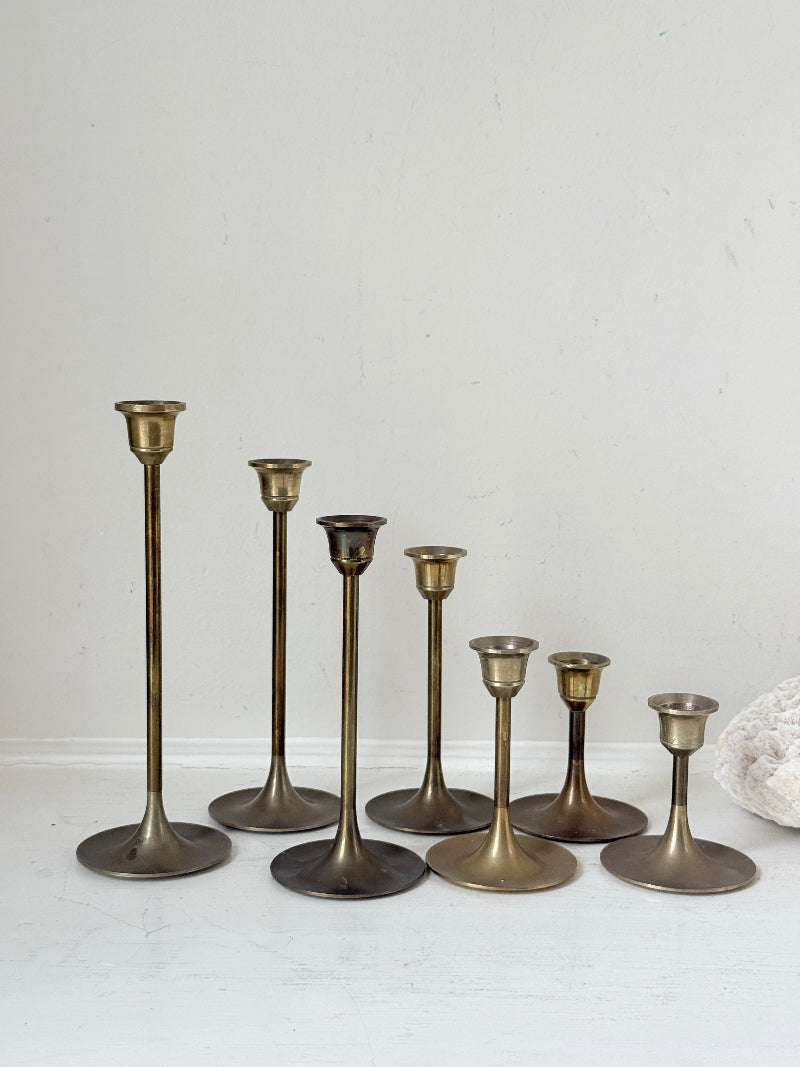 Set of 7 vintage brass candlesticks in graduated heights with aged brass finish styled with red ribbon on white surface