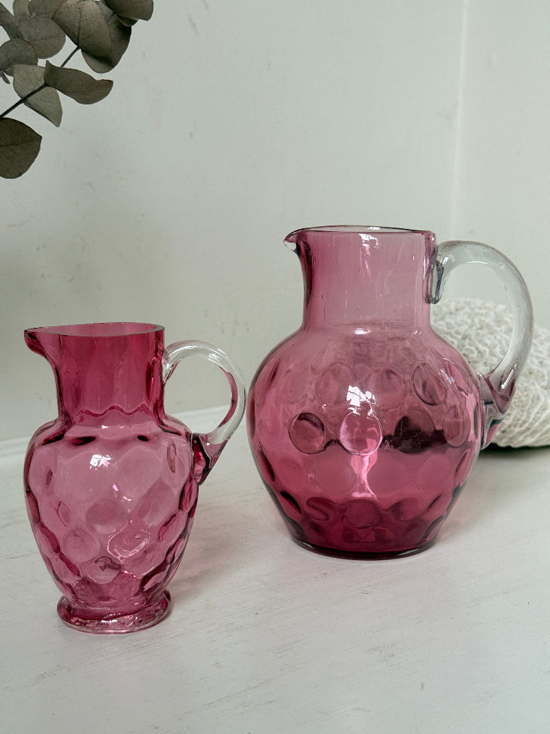 Vintage cranberry glass jugs, a pair with clear handles, photographed on a white surface