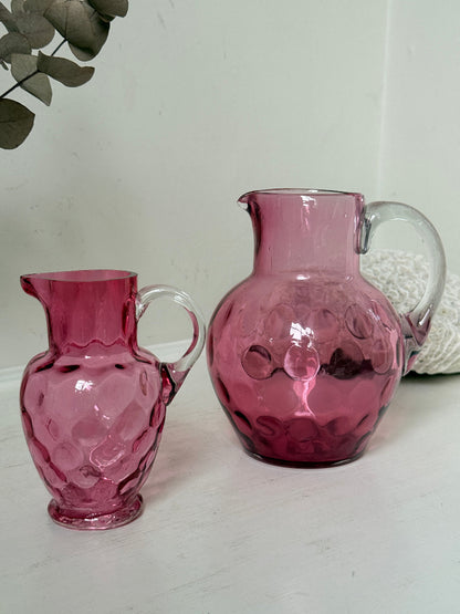 Vintage cranberry glass jugs, a pair with clear handles, photographed on a white surface