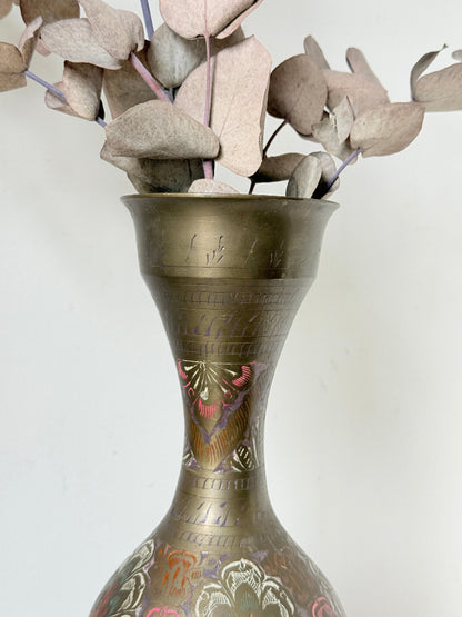 Vintage Indian engraved brass vase with enamel floral decoration and aged patina styled with dried stems on white surface