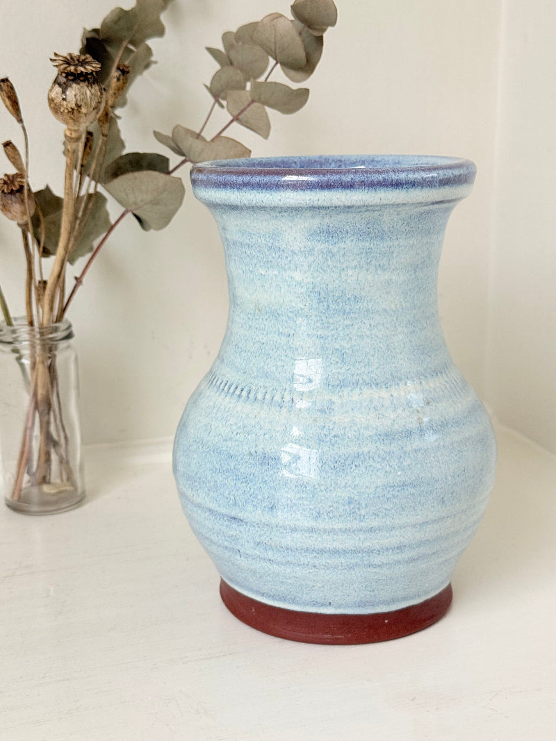 Studio pottery vase with sky blue glaze, indigo rim, and natural red clay base, photographed on a white surface