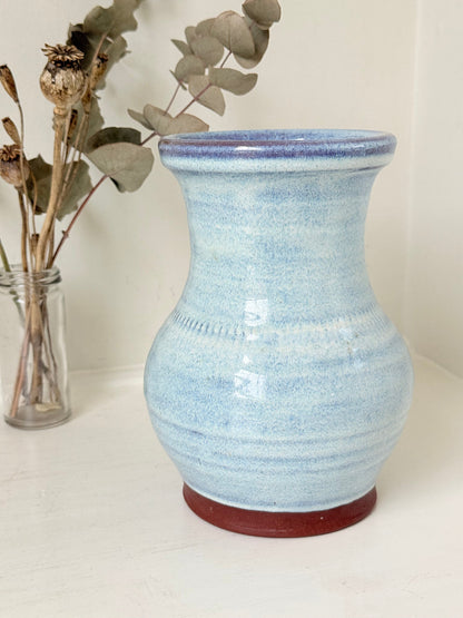 Studio pottery vase with sky blue glaze, indigo rim, and natural red clay base, photographed on a white surface