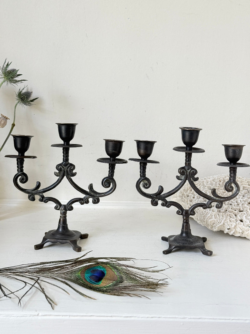 Pair of vintage brass three arm candelabra with scrolling arms and aged patina, photographed on a white surface