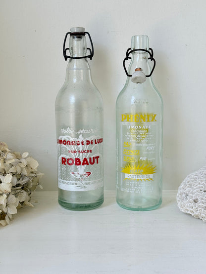 Pair of vintage French glass bottles with retro typography and graphics, photographed on a white surface